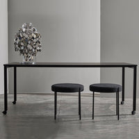 Sleek black dining table and two matching round stools on a light grey floor, complemented by a silver decorative vase.