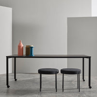 Sleek black table with two round black stools; features colorful decor in pink, blue, and yellow against a minimalist backdrop.