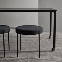 Black modern table with sleek design and two round black fabric stools on a textured gray floor.