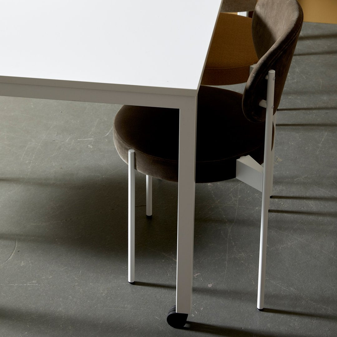 White table with a sleek design and dark brown upholstered chair against a textured gray floor.