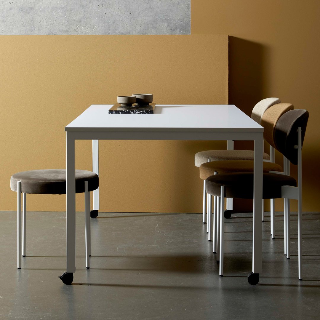 White table with sleek design, paired with brown and beige patterned chairs against a warm, earthy backdrop.