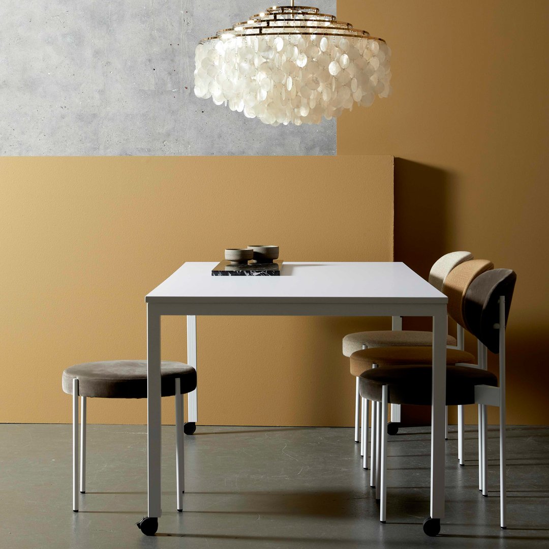 Stylish white dining table with patterned beige and brown chairs, set against a warm, golden-orange wall.