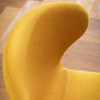 Curved yellow chair upholstered in soft fabric with a smooth texture against a wooden floor.