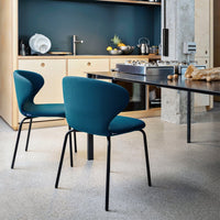 Teal upholstered chairs with smooth curves and black legs, set against a modern kitchen backdrop.