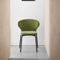 Green velvet chair with a smooth finish and sleek black legs, set against a minimalist backdrop.