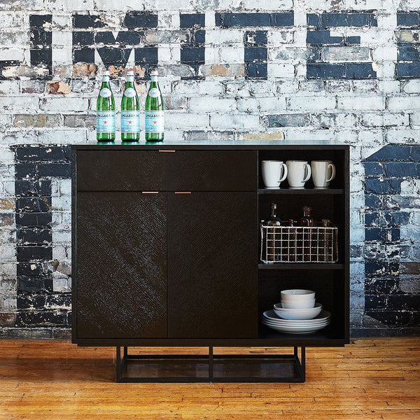Modern black cabinet with textured pattern, featuring a matte finish and sleek metal accents against a rustic backdrop.