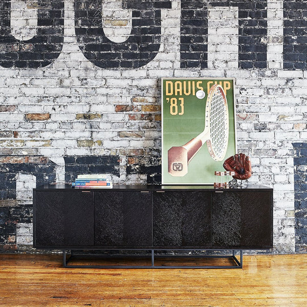 Black-patterned cabinet against a rustic brick wall with wooden floor, featuring a vintage poster and decorative items.