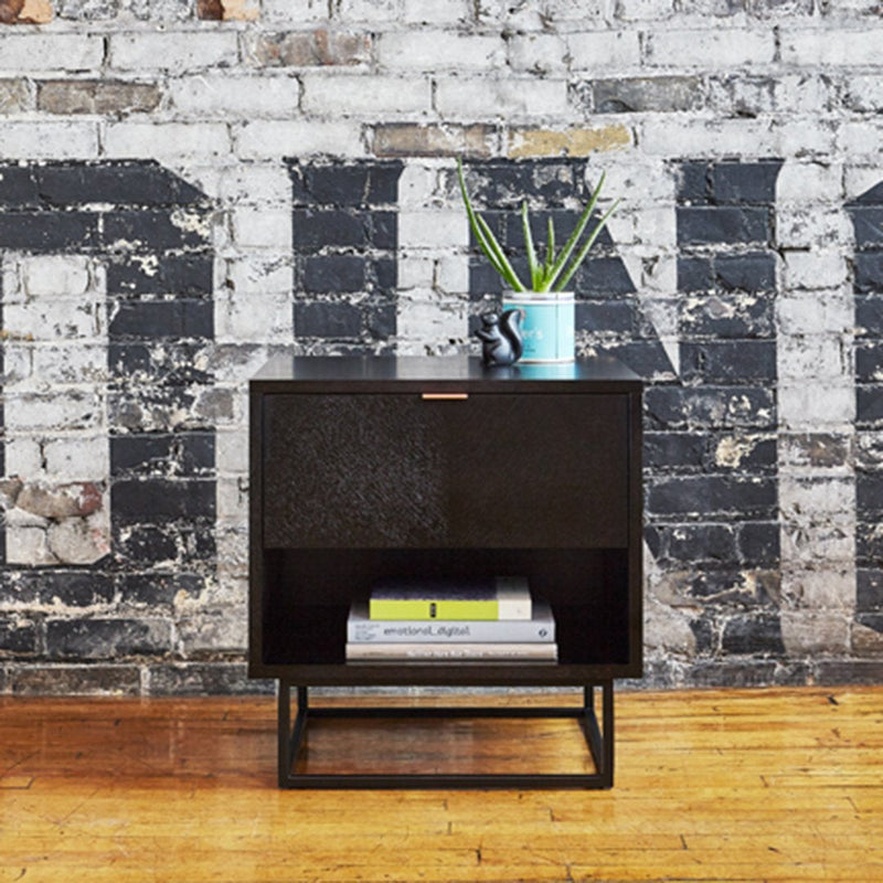 Black nightstand with a textured surface, featuring a sleek design against a rustic brick wall.