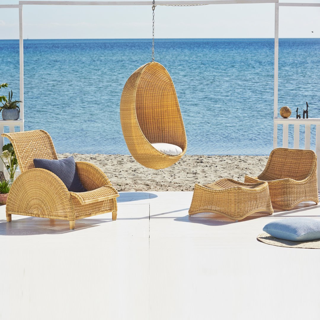 Natural rattan chairs and hanging pod in warm beige tones, set against a serene blue ocean backdrop. Perfect for coastal decor.