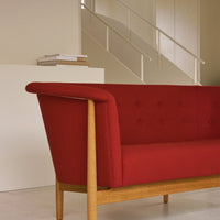 Red sofa with tufted fabric and natural wooden legs, featuring a minimalist design against a neutral background.