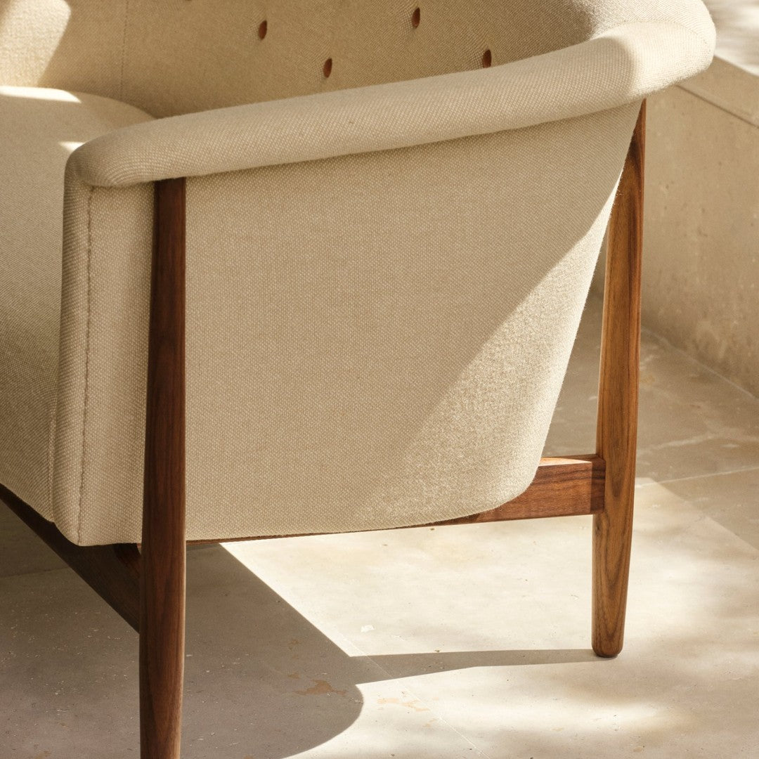 Beige upholstered armchair with a textured fabric and rich wooden legs, featuring a minimalist design and soft curves.