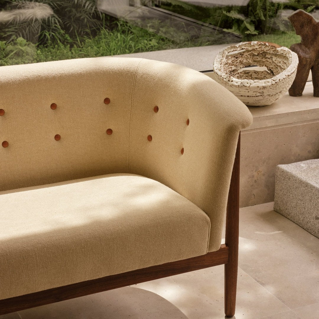 Beige curved sofa with tufted buttons and dark wood legs, blending modern design with natural tones.