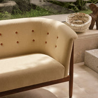 Beige curved sofa with tufted buttons and dark wood legs, blending modern design with natural tones.