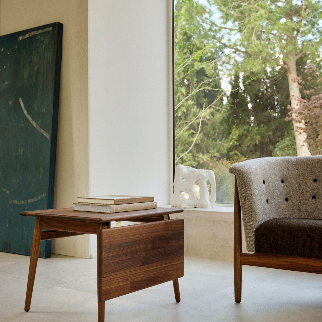 Modern walnut side table with natural wood grain, paired with a textured gray and beige upholstered chair.