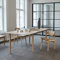 Light wood dining table with minimalist design, paired with natural wood chairs in a bright, airy room.