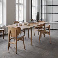 Light wood dining table with beige upholstered chairs, set against a neutral gray floor and bright, airy windows.