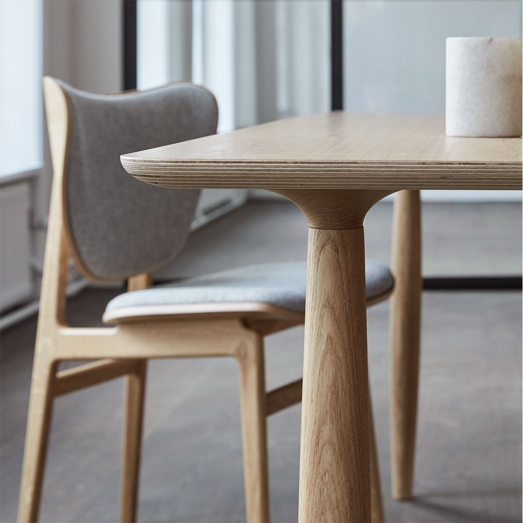 Wooden dining table with light oak finish, complemented by a gray upholstered chair, featuring clean lines and minimalistic design.