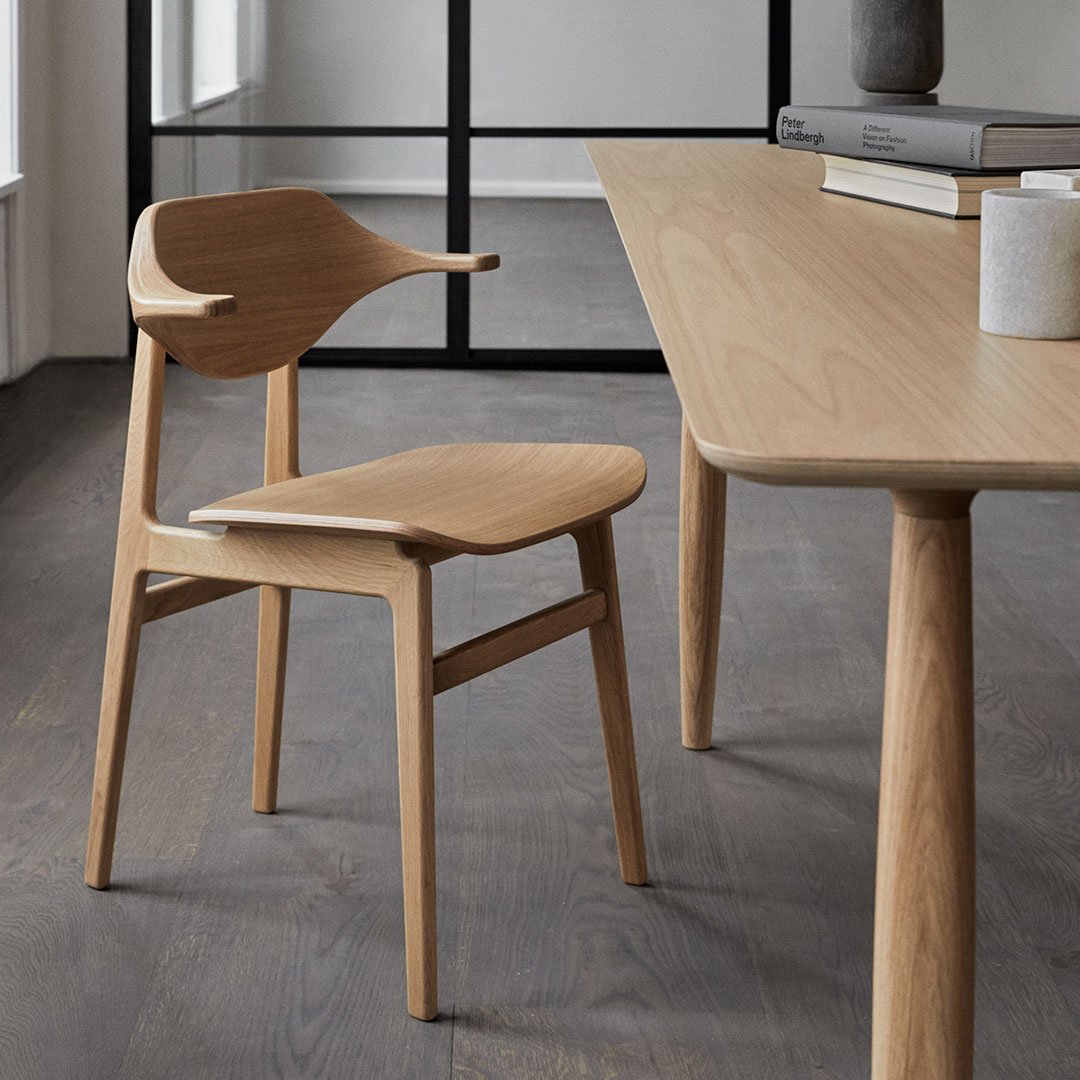 Natural light oak chair with smooth curves and a minimalist design, set against a contemporary, neutral-toned backdrop.