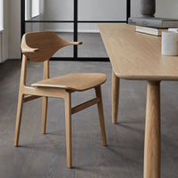 Natural light oak chair with smooth curves and a minimalist design, set against a contemporary, neutral-toned backdrop.