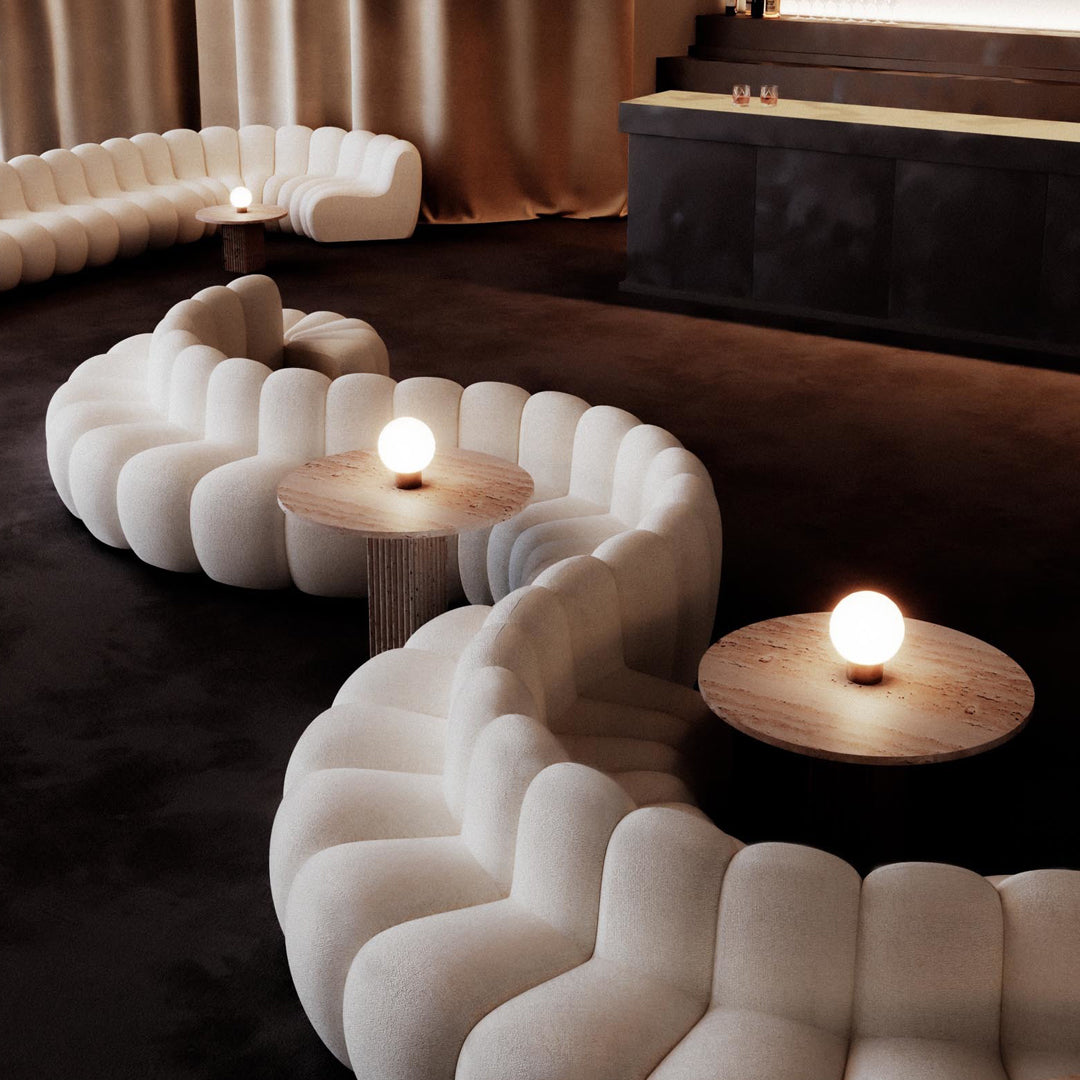 Curved white sofa with soft, plush fabric and round wooden tables in a warm, neutral-toned living space.