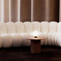 Curved white sofa with plush texture, paired with a wooden table on a rich brown carpet backdrop.