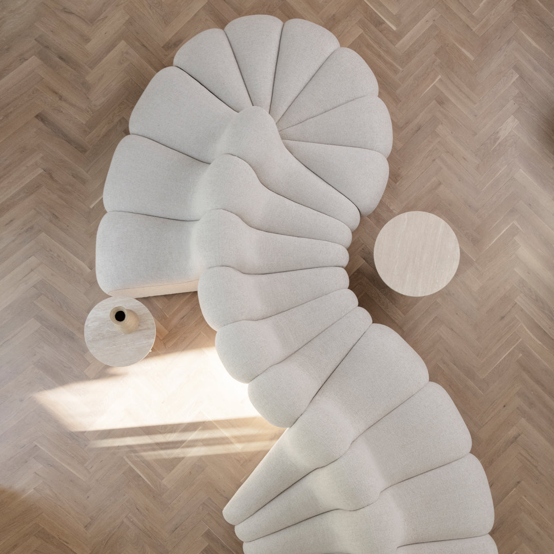Cream-colored curved sofa with a textured, wave-like pattern, paired with a round wooden table on herringbone flooring.