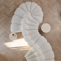 Cream-colored curved sofa with a textured, wave-like pattern, paired with a round wooden table on herringbone flooring.