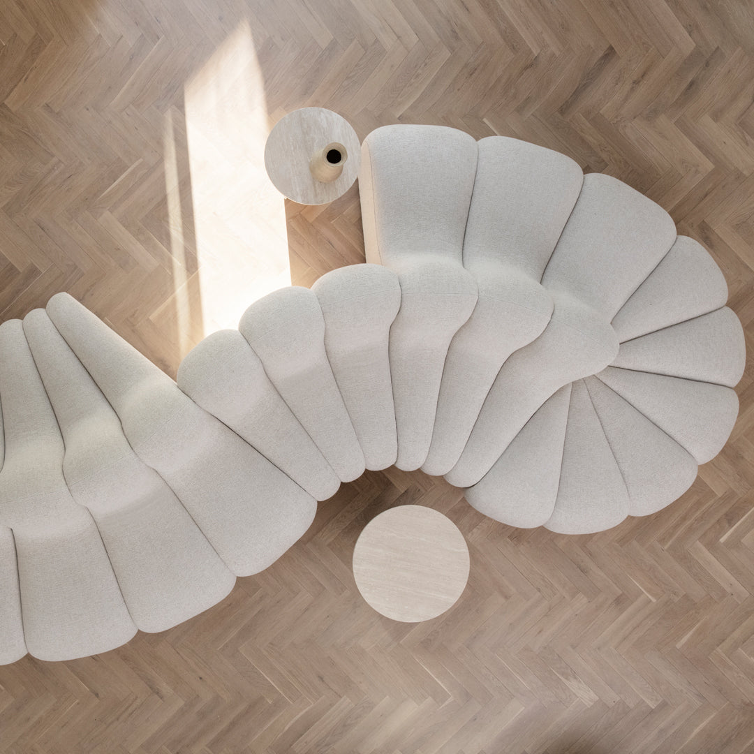Modern cream-colored sofa with petal-like curves, set against a herringbone wood floor. Elegant and stylish design.