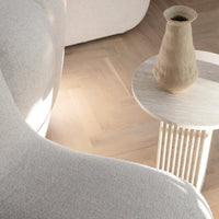 Neutral beige curved sofa with textured upholstery, light wood flooring, and a minimalist round side table in soft tones.