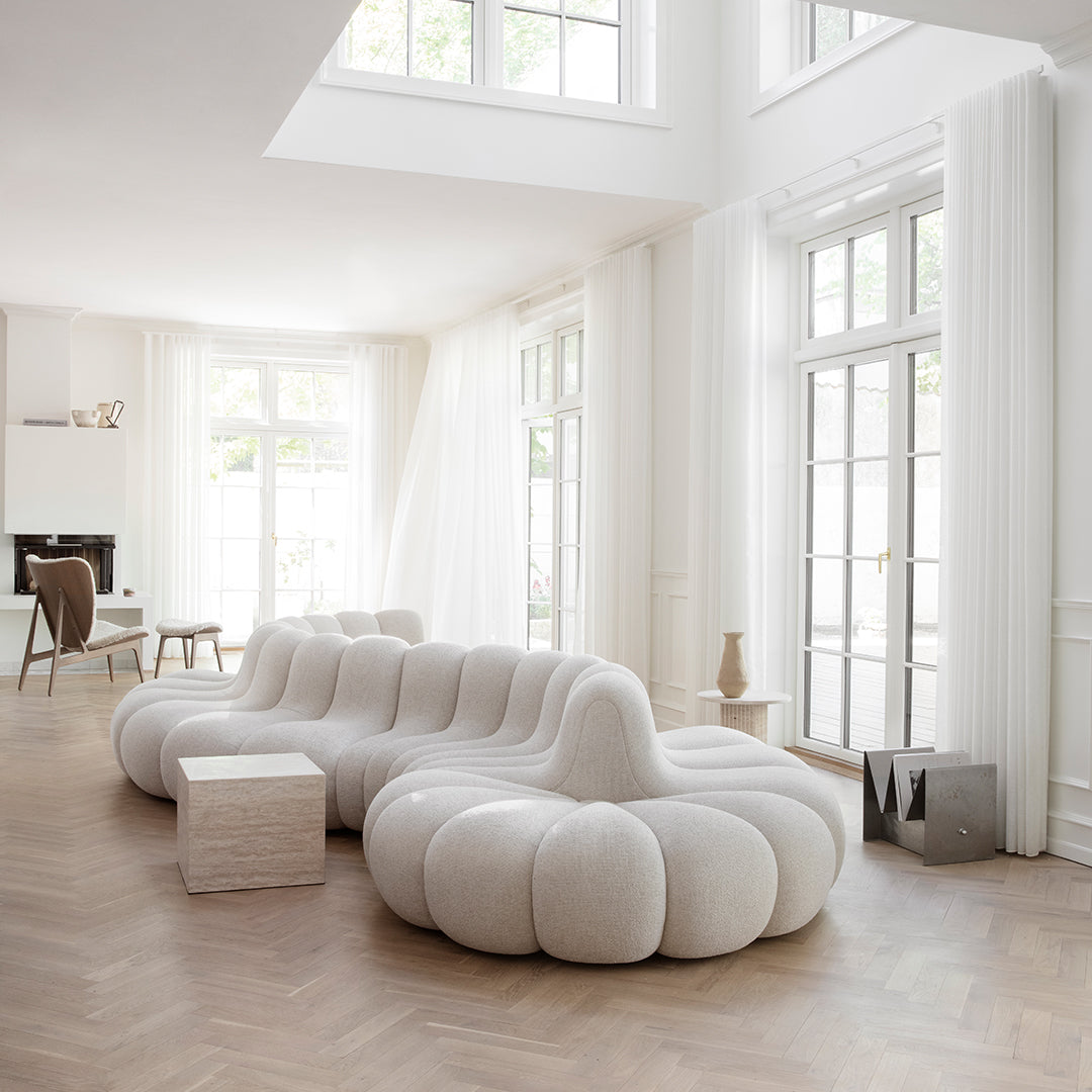 White tufted modular sofa in a bright, airy room with large windows and light wood flooring. Modern, minimalist design.