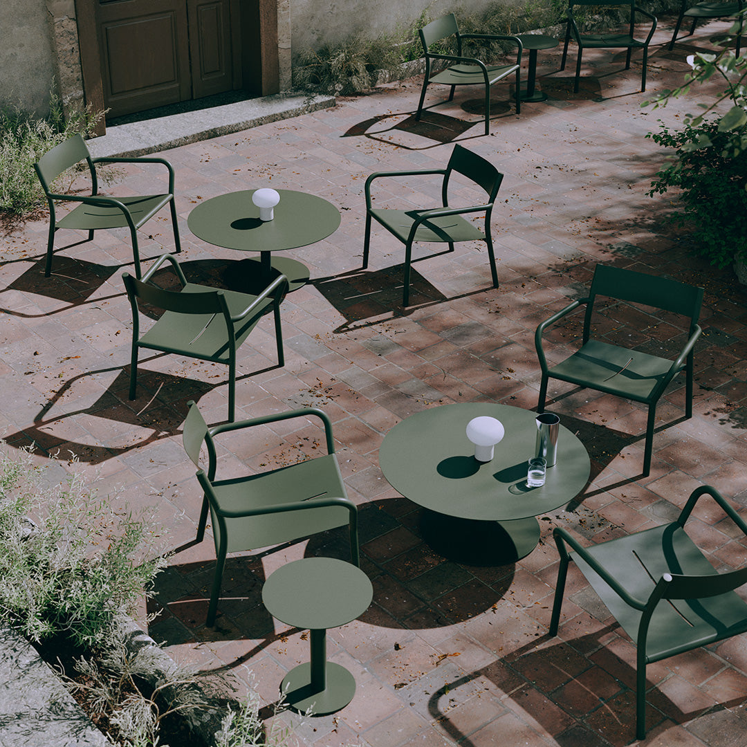 "Green outdoor chairs and tables on a rustic brick patio, featuring minimalist designs and subtle natural patterns."
