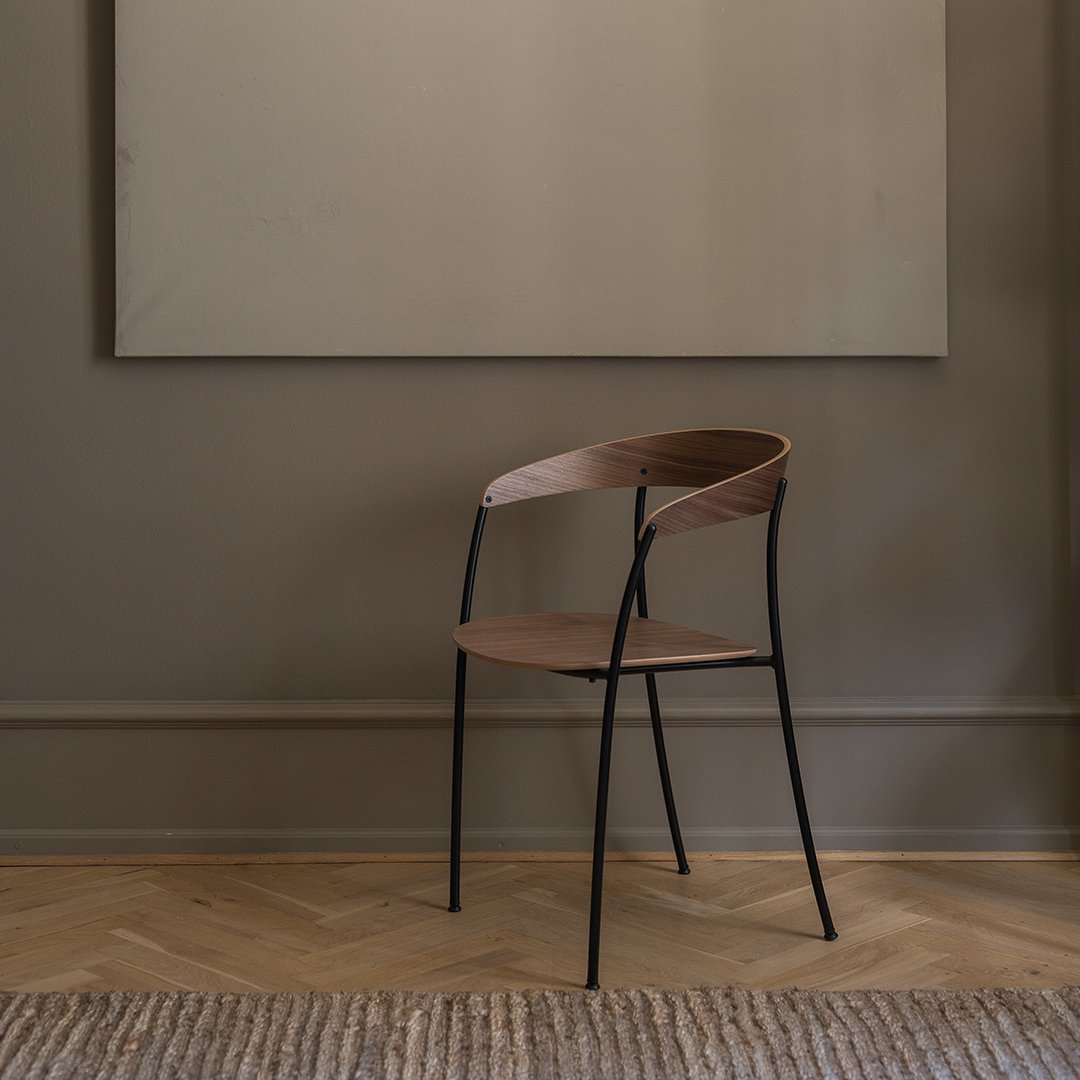 Wooden chair with a sleek brown seat and backrest, complemented by black metal legs in a minimalist setting.