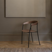 Wooden chair with a sleek brown seat and backrest, complemented by black metal legs in a minimalist setting.