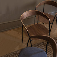 Stylish wooden chairs with curved backs, featuring a rich brown finish and sleek black metal legs on a light wooden floor.