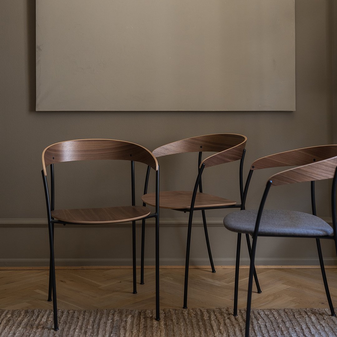 Wooden and grey upholstered chairs with sleek black metal legs against a neutral wall and textured rug. Stylish and modern.