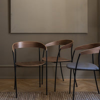 Wooden and grey upholstered chairs with sleek black metal legs against a neutral wall and textured rug. Stylish and modern.