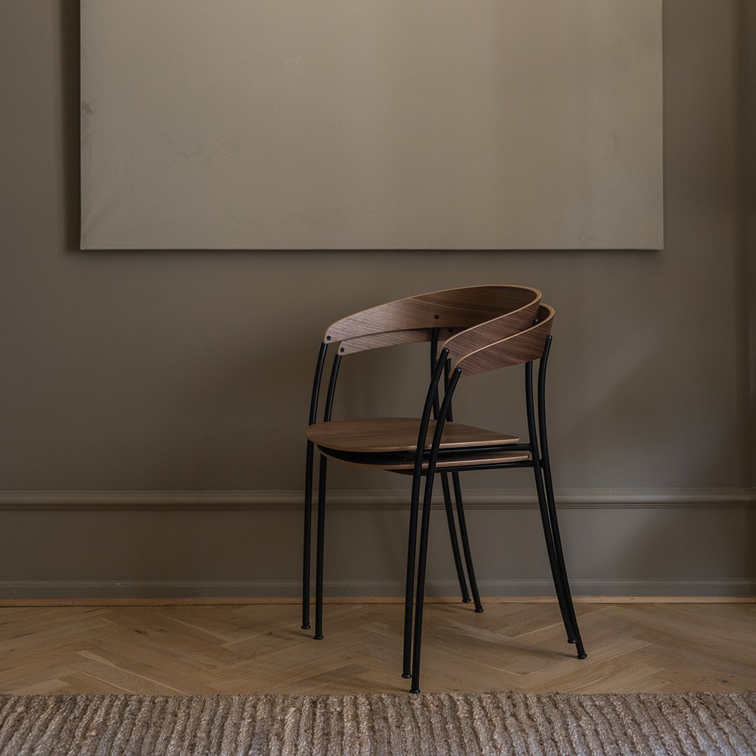 Wooden chair with a rich brown finish and sleek black legs, set against a neutral wall and light wood floor.