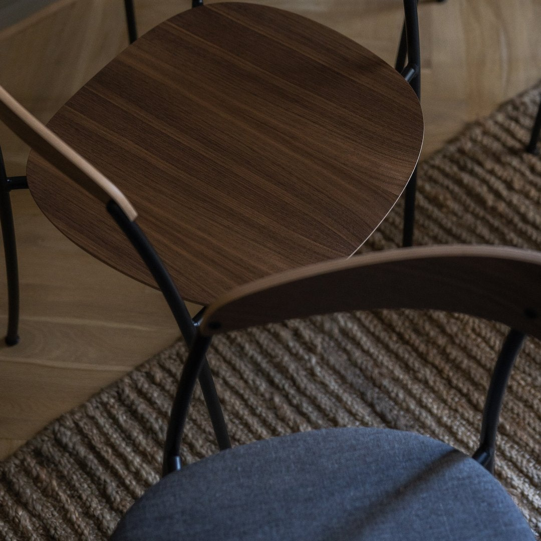 Brown wood table with black metal legs alongside a gray fabric chair on a textured beige rug.