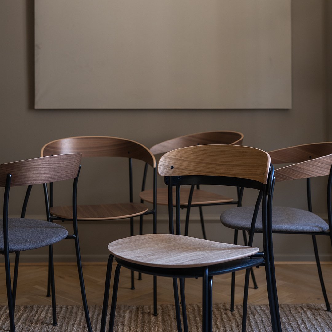 Set of modern chairs with natural wood finishes and dark metal frames on a textured floor, against a neutral backdrop.
