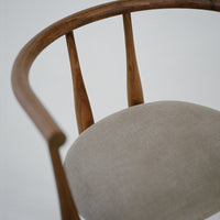 Close-up of a wooden chair with a beige cushion on a plain background