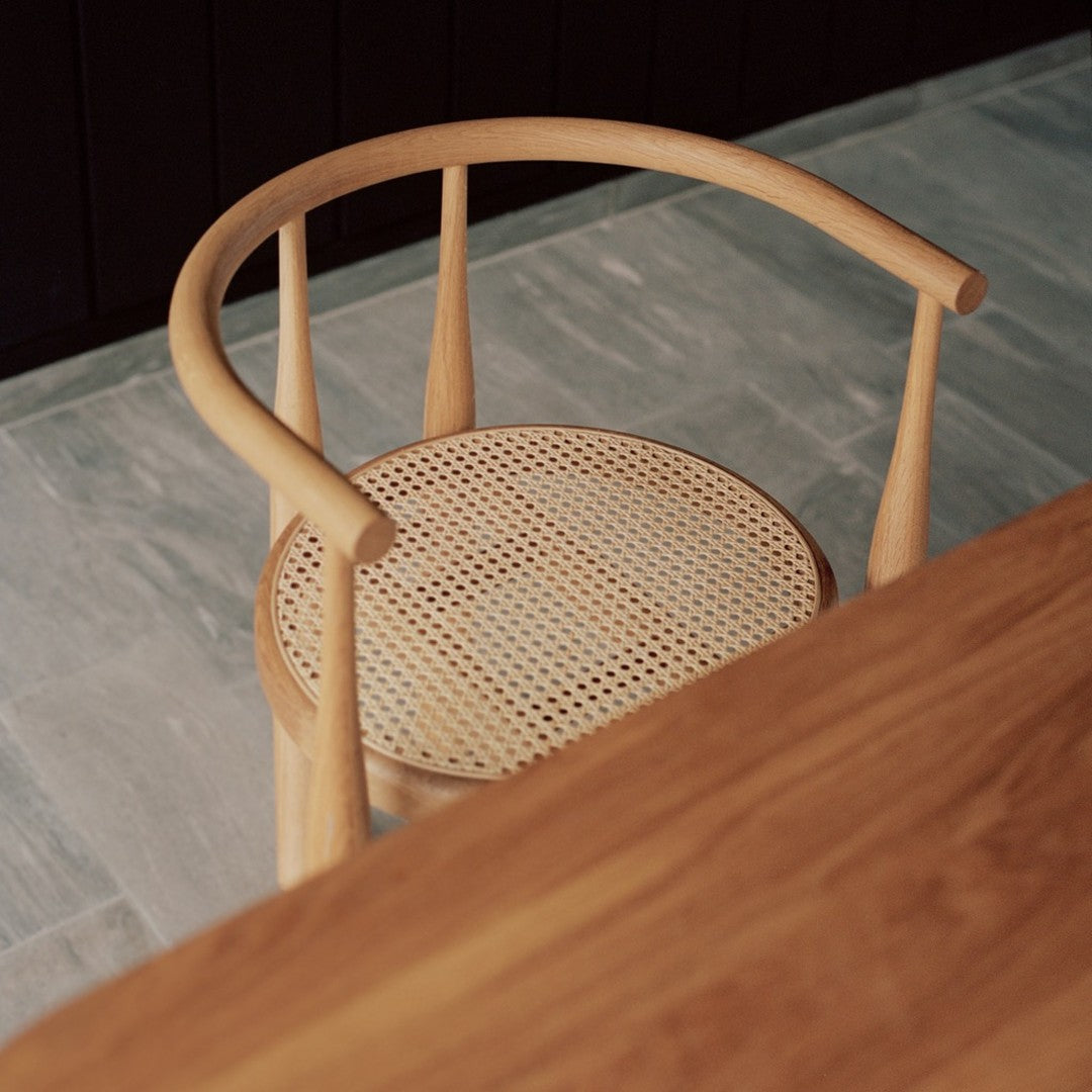 Natural wood chair with a light tan finish and woven caning pattern on the seat, set against a gray stone floor.