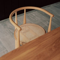Natural wood chair with a light tan finish and woven caning pattern on the seat, set against a gray stone floor.