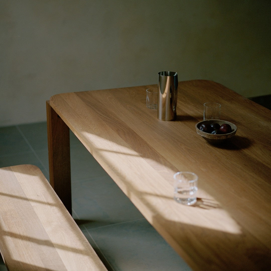 Natural wood tones with a sleek silver accent, complemented by dark fruits in a simple bowl on a minimalist surface.