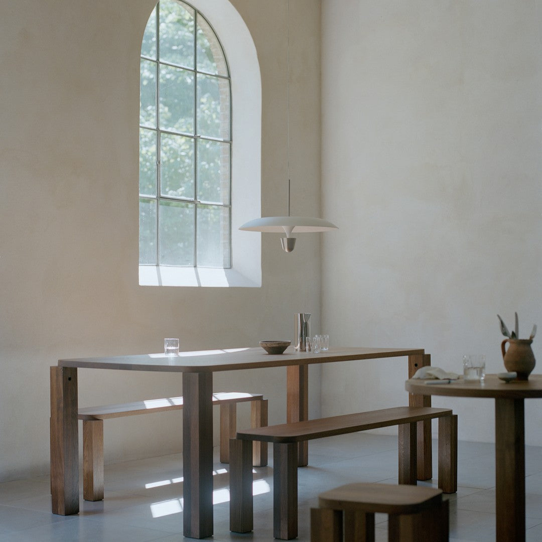 Minimalist wooden table and benches in rich brown tones, paired with a sleek white pendant light in a softly lit room.