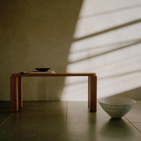 "Light wood table with a dark bowl, white textured bowl, and gray stone floor against a soft beige wall, creating a warm aesthetic."
