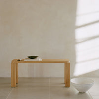Light wood bench with a minimalist design against a textured beige wall and soft gray tiles.