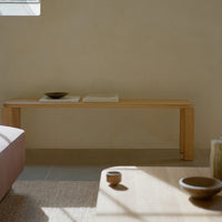 Natural wood bench in light oak color, with soft textures and minimalist design, set against a neutral wall backdrop.