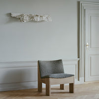 Grey textured chair with natural wood legs against a soft, neutral wall, featuring a minimalist design.