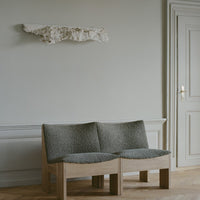 Gray textured upholstery on a modern wooden bench against a neutral beige wall and light wood flooring.