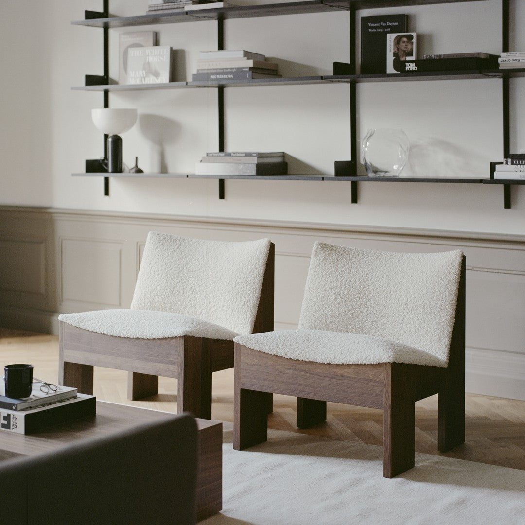 Two cozy chairs featuring soft white upholstery and rich wooden frames, set against a neutral-colored backdrop.